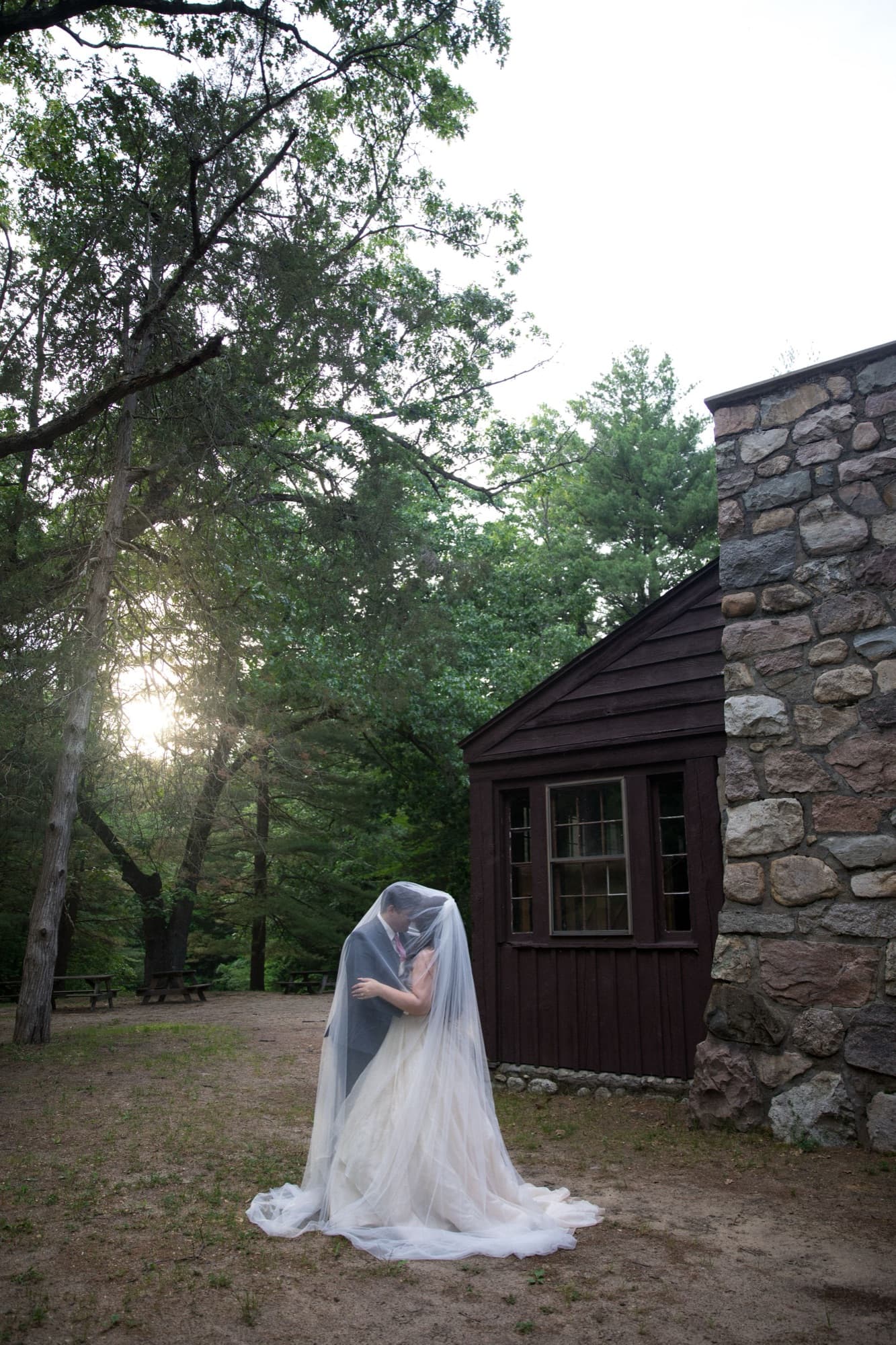 A bride under her veil beside a stone-chimney cabin in the pines