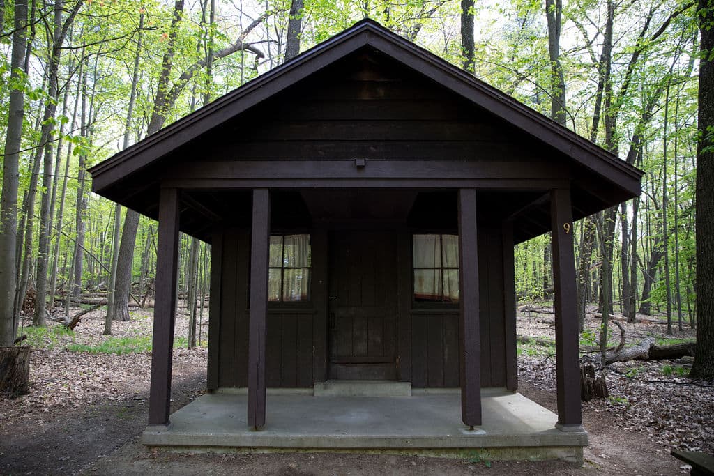 Dark-stained CCC cabin with a covered porch in the spring woods