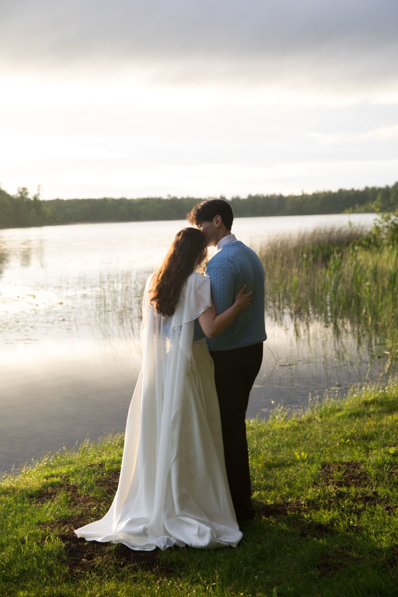 A bride and groom on the grassy shore of Long Lake at sunset